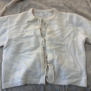 Vit kofta med snörning från Gina Tricot - Superfin vit kofta från Gina Tricot i ullblandning. Koftan har snygg snörning framtill istället för knappar och är ribbstickad vid hals, ärmslut och nederkant. Använt 1 gång, så den är nästintill helt ny!