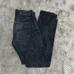 Svarta jeans från Nudie Jeans - Svarta skinny jeans från Nudie Jeans med coolt marmorerat mönster. Klassisk femficksmodell, smal passform och normal midja. Jeansen är gjorda i stretchig bomull för extra komfort och har Nudie-logga på bakfickan.