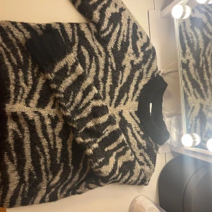 Zebramönstrad stickad tröja från Vila - Säljer en stickad tröja från Vila med svart och beige zebramönster. Tröjan har rund halsringning, ribbade muddar och långa ärmar. Perfekt för dig som vill sticka ut med ett djurmönster och hålla dig varm under kyliga dagar.