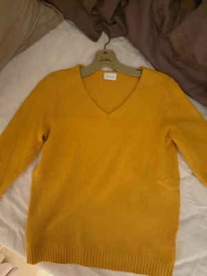 Gul v-ringad tröja från Vila - Mysig gul tröja från Vila med v-ringning och långa ärmar. Tröjan har ribbade muddar vid ärmslut och nederkant, perfekt för lager på lager under höst och vår. Enkel och stilren design som passar till det mesta.