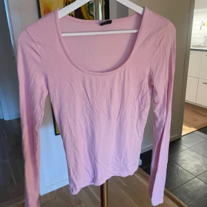 Ljusrosa långärmad topp Gina Tricot - En enkel och stilren ljusrosa långärmad topp från Gina Tricot. Toppen har rundad urringning och är gjord i ett mjukt bomullsmaterial som känns skönt mot huden. Perfekt att matcha med jeans eller kjol för en clean look.