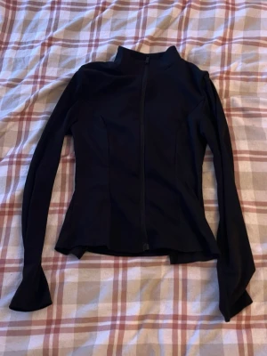 Svart zip-kofta från SHEIN XS - Säljer en svart, figurnära kofta från SHEIN i storlek XS. Tröjan har hel dragkedja framtill, hög krage och långa ärmar. Sidorna har ribbade paneler som ger en snygg kontrast. Perfekt till lager på lager och enkel att styla.