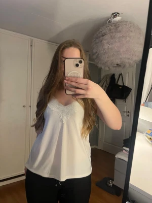 Vit linnetopp med spets från Amisu - Säljer en vit linnetopp från Amisu med tunna axelband och v-ringning dekorerad med spets. Toppen är i ett mjukt, lätt material och har en avslappnad passform. Perfekt för varma dagar eller att styla lager på lager.