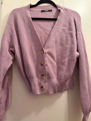 Ljuslila ribbad kofta från BikBok - Superfin ljuslila kofta från BikBok i ribbad stickad kvalitet. Koftan har v-ringning, långa ärmar och snygga knappar framtill. Croppad modell som passar perfekt till både jeans och kjol. Enkel att styla för en trendig look.