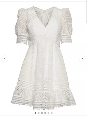 Vit spetsklänning By Malina - Supersöt vit kortklänning från By Malina med v-ringning, puffärmar och spetsdetaljer. Klänningen har broderade blommor, prickigt mönster och volangkant nertill. Dragkedja bak och fodrad insida. Perfekt för sommarens alla tillfällen! Köpte för 2600kr går ej att få tag på längre. Använd endast en gång. 