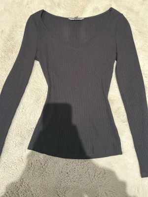 Svart ribbad topp från H&M - Säljer en svart långärmad topp från H&M i storlek XS. Toppen är ribbad med v-ringad hals och har en slim passform som sitter snyggt på kroppen. Perfekt basplagg till garderoben och lätt att styla med olika outfits. Som sagt den har fått hänga med ut ur min rensning från garderoben som bara har hängt där. Den är knappt använd och är i bra skick. Fläcken man ser på ena armen tar vi bort innan vi skickar iväg den
