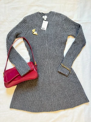 Mörkgrå ribbstickad klänning – figurnära & stilren (nyskick) från H&M - •En mörkgrå ribbstickad klänning. •I figurnära modell. •Helt oanvänd med lapp kvar. •Ribbstickat material som ger en smickrande silhuett. •Stretchigt och bekvämt tyg. •Perfekt längd att bära med boots, klackar eller sneakers. •Smyckena och väskan följs inte med - de visas endast i den första bilden som tips om hur klänningen kan stylas. •Passar bra till kallare vinter och vår dagar.   Storlek och mått: •Storlek S. •Bröstmått: 80cm (40cm x 2). •Längd: 84cm.