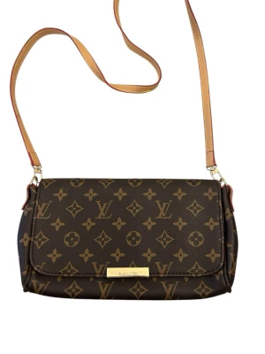 Väska - Säljer en klassisk axelväska med ikoniskt monogrammönster i brunt och beige. Väskan har justerbar axelrem i ljust skinn och insida i röd mocka. Perfekt storlek för det viktigaste och en snygg detalj till din outfit.