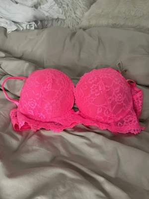 Neonrosa spets-bh med vaddering - Snygg neonrosa bh med vadderade kupor och justerbara axelband. Bh:n är täckt av blommig spets och har fina spetsdetaljer längs kanterna. Perfekt för dig som vill ha något färgstarkt och extra.