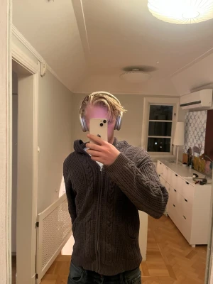 Grå stickad hoodie med dragkedja - Mysig grå stickad hoodie med dragkedja framtill och huva. Snyggt flätmönster över hela tröjan och två fickor fram. Storleken säger XL men jag tycker den passar M. Modellen är 185cm