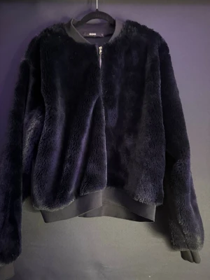 Svart teddyjacka från BikBok - Mysig svart teddyjacka från BikBok i storlek L. Jackan har en mjuk, fluffig yta och stängs med dragkedja framtill. Ribbad mudd vid hals, ärmslut och nederkant ger en snygg och bekväm passform. Perfekt för kalla dagar när du vill vara både varm och stilren.