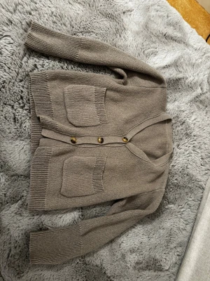 Beige stickad kofta / cardigan - Mysig beige stickad kofta med v-ringning och tre knappar framtill. Två stora fickor på framsidan och ribbade muddar vid ärmslut och nederkant. Köpt second hand så vet tyvärr inte märket, och skulle gissa på att storleken är S - M!!