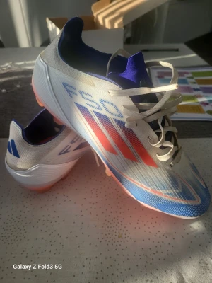 Adidas F50 fotbollsskor blå/vit/röd - Säljer ett par Adidas F50 fotbollsskor i vitt med blå och röda detaljer. Skorna har snörning, låg profil och en lätt syntetisk ovandel. Använda fåtalgånger och i väldigt fin skick.