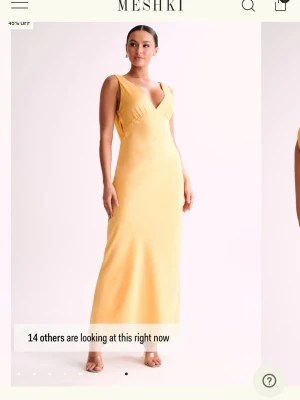 Gul långklänning från Meshki - Supersnygg gul långklänning från Meshki i ett glansigt satinliknande material. Klänningen har djup v-ringning, smala axelband och en öppen rygg med draperad detalj. Perfekt för dig som vill sticka ut med en elegant och modern look. Storleken är xs och den går ner till fötterna på mig som är 169. Den är större i storleken o sitter som en S, den sitter inte heller jätte tajt runt mag området men inte heller löst för dig som gillar de ❤️