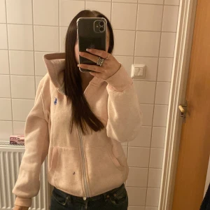 Rosa ralph lauren zip hoodie - Ljus rosa ralph lauren zip hoodie i storlek M, men den sitter som en Xs/S då den är liten i storlek! Dock är det en liten mascara ” fläck” på den som inte går bort darför säljer jag den billigt men pris kan diskuteras!