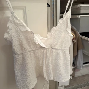 Vit linnetopp med volang och knyt - Söt vit linnetopp med tunna axelband, volangkant och knyt framtill.💗