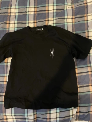 Svart Amiri t-shirt med tryck - Säljer en svart t-shirt från Amiri med unikt grafiskt tryck i vitt och grått på både bröstet och ryggen. T-shirten har klassisk passform och är gjord i mjuk bomull. Väldigt bra skick på T-shirten. Minimal användning!