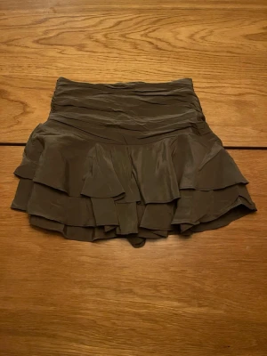 Grön volangkjol från Zara XS - Supersöt grön kortkjol från Zara i storlek XS. Kjolen har flera lager volanger som ger en flowy känsla och är tillverkad i ett mjukt, tunt material. Perfekt för dig som vill ha en feminin och trendig look. De har även inbyggda shorts under!!! Använda en gång helt nya!!!