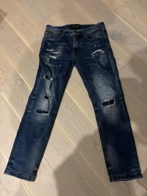 Blå ripped jeans Supply & Demand XS - Säljer ett par blå jeans från Supply & Demand med snygga slitningar och hål på benen. Modellen har klassisk femficksdesign, dragkedja vid fickan och skinny passform. Perfekta för dig som gillar en edgy streetstil.