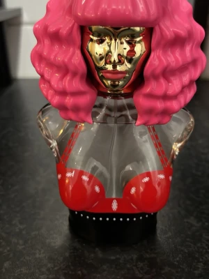 Nicki minaj parfym - Parfymflaska formad som en byst med rosa hår och guldfärgat ansikte. Volym: 100 ml. Tillverkad i USA. Perfekt för dig som vill sticka ut med en cool och kreativ design på parfymhyllan.