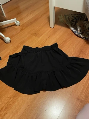 Svart volangkjol med resårmidja - Säljer en svart kortkjol med bred volangkant och resår i midjan. Kjolen har en enkel och flowy design som ger en snygg siluett. Perfekt för dig som gillar en basic men ändå trendig look. Materialet känns som bomull och är mjukt mot huden. Från Lindex