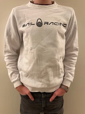 Vit Sail Racing sweatshirt - Tjena! Säljer  en vit sweatshirt från Sail Racing med svart logga och text framtill. Klassisk rund halsringning och ribbade muddar vid ärmslut och nederkant. Tillverkad i mjuk bomulls- och polyestermix för skön känsla. Perfekt till chill vardagsstil. Storleken på tröjan är 150 cm. Vid minsta funderingar är det bara att skriva. Pris kan diskuteras!