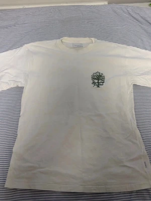 Vit t-shirt Vailent Burning Palms S - Säljer en vit t-shirt från Vailent i storlek S med grön tryckt Burning Palms-grafik på ryggen och ett mindre palmtryck fram. Skön bomullskänsla och klassisk passform med korta ärmar. Använd men väldigt fräsch och inga fläckar på eller slitage vad jag kan se. Perfekt för dig som gillar coola prints och streetwear vibes. Diskuterar gärna pris!