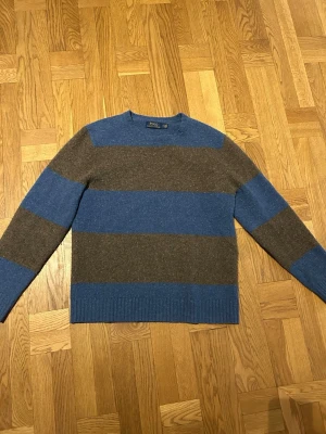 Blå-Brun-Randig Kashmir och ull tröja från Polo Ralph Lauren - Säljer en randig tröja från Polo Ralph Lauren i blått och brunt. Tröjan har breda ränder, ribbade muddar och bruna mockalappar på armbågarna. Ull och kashmirblandning