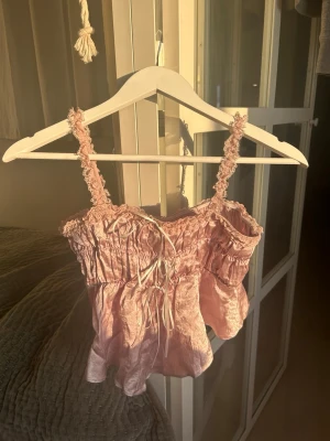 Pyjamas set i satin - Supergulligt pyjamas set med silkes liknande material som passar i olika tillfällen. Toppen kan användas som en sommartopp. Setet är i ljusrosa med vita och rosa lace-detaljer. Köpt i Tokyo, från butik Beams LiloCilly.   Storlek S/Xs. Resår gör byxorna och toppen stretchiga. Toppen är ca 33cm lång fram och baktill.  Men den är asymmetrisk (sidorna är ca 23 cm långa). Se bild 5.  Byxorna är ca 100cm långa från toppen till botten. Innerbensmåttet är ca 66 cm.  #sommartopp #satintopp #satinpyjamas