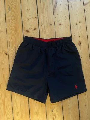 Mörkblå badshorts från Ralph Lauren - Säljer ett par mörkblå badshorts från Ralph Lauren i storlek M. Shortsen är i nyskick, 10/10, och endast provade en gång. Säljes då de tyvärr är för små. Nypris ca 1 000 kr. Klassisk modell med bra passform och fin kvalitet.  Hör av dig vid frågor eller för fler bilder. Pris kan diskuteras vid snabb affär.