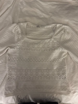 Vit stickad topp från ONLY - Säljer en vit stickad topp från ONLY med vackert spetsmönster och strukturstickade detaljer. Toppen har trekvartsärm och fyrkantig ringning, vilket ger en trendig och fräsch look. Perfekt att styla med jeans eller kjol för en cool outfit.