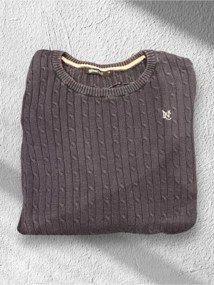 Mörkgrå kabelstickad tröja Gina Tricot - Säljer en mörkgrå kabelstickad tröja från Gina Tricot i storlek XS. Tröjan har rund halsringning, ribbade muddar och ett broderat emblem på bröstet. Perfekt för lager på lager under höst och vinter.