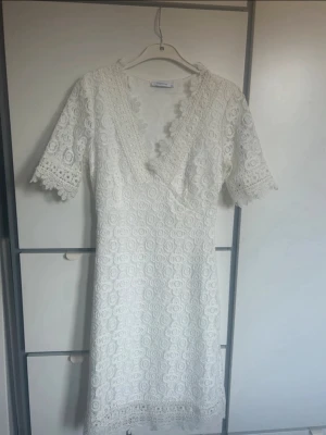 Vit spetsklänning från Reserved XS - Supersöt vit spetsklänning från Reserved i storlek XS. Klänningen har v-ringning, korta ärmar och fina spetsdetaljer över hela plagget. Perfekt till sommaren med sitt blommiga mönster och romantiska look. För student eller avslutning.