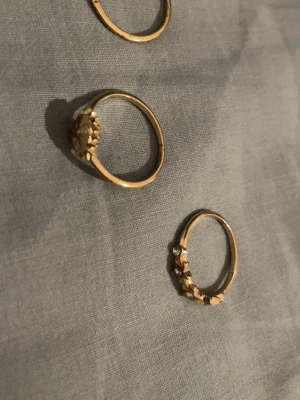 Guld ringar - De här vackra ringarna i guld är en perfekt blandning av elegans och charm. De pryds med gnistrande stenar och har en unik design som gör den till ett blickfång. Perfekt för både vardag och fest. I storlek S/M tre stycken 
