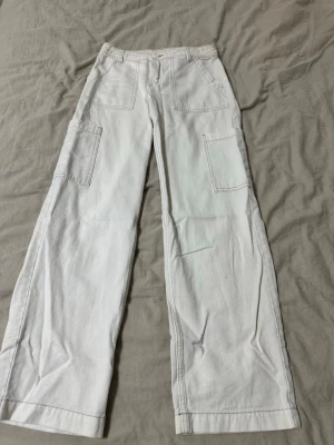 Vita cargopants med raka ben - Säljer ett par vita cargopants med raka ben och stora fickor på sidorna. Byxorna har mid midja och är tillverkade i ett kraftigare bomullstyg. Snygga kontrastsömmar och klassisk cargostil som passar till många olika looks.