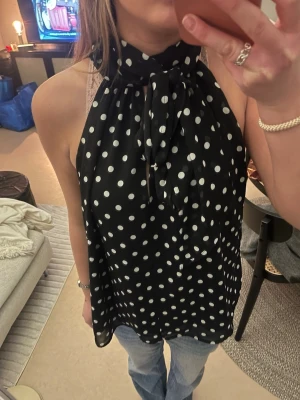 Svart prickig halterneck blus H&M - Säljer en svart halterneck blus från H&M med vita prickar och stor knytrosett i halsen. Lappen är borta men det är storlek S. 