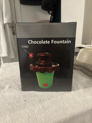 Röd och brun chokladfontän - Säljer en chokladfontän med röd plastkropp och brunt lock och topp. Fontänen drivs av 4 C-batterier (ingår ej) och är enkel att montera. Perfekt för att smälta och servera choklad på ett kul sätt. Höjd ca 20 cm.