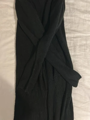 Svart lång kofta från Friends - Lång svart Koftan är stickad och har långa ärmar, perfekt för lager på lager under kyliga dagar. Enkel och stilren design som passar till allt. 