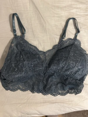 Mörkblå spetsbralette med justerbara band - Säljer en mörkblå bralette med vackra spetsdetaljer och blommigt mönster. Den har justerbara axelband och bred spetskant nedtill. Perfekt för att ge en extra touch till din outfit.