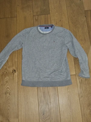 Grå sweatshirt från GANT - Klassisk grå sweatshirt från GANT med rund halsringning och diskret logga på bröstet. Tröjan har ribbade muddar vid ärmslut och nederkant. Perfekt till chill dagar och enkel att matcha med jeans eller joggers.