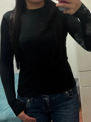 Svart långärmad polotopp - Säljer en svart långärmad polotopp i stretchigt material. Toppen har en enkel och clean design med hög hals och figurnära passform. Perfekt att styla med jeans eller kjol för en snygg och stilren look.