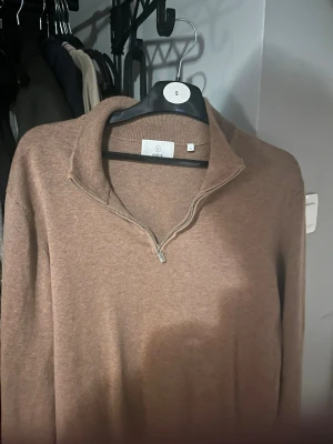 Beige stickad tröja med half zip från Bläck - Mysig beige stickad tröja från Bläck i storlek S. Tröjan har en stilren half zip-dragkedja vid kragen och är långärmad. Perfekt för lager-på-lager under höst och vinter. Enkel att matcha med jeans eller chinos.