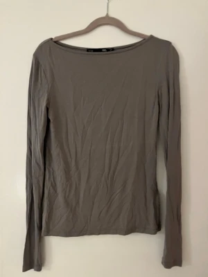 Grå långärmad topp från 157 - En enkel och stilren grå långärmad topp från 157 i storlek XS. Toppen har rund halsringning och är gjord i ett mjukt och stretchigt material som känns skönt mot huden. Perfekt att matcha med jeans eller kjol för en clean look.