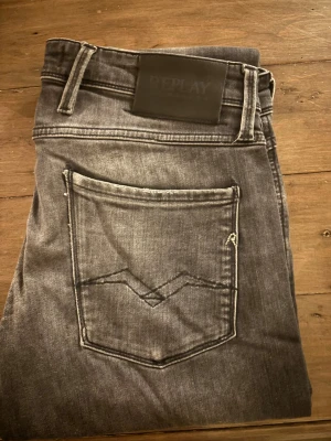 Replay grå jeans slim fit - Säljer ett par gråa Replay jeans i slim fit med snyggt slitna detaljer och klassisk femficksmodell. Jeansen har svarta sömmar, Replay-logga på bakfickan och är tillverkade i mjukt denimtyg. Perfekta för dig som gillar en smalare passform och stilren look.