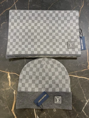 Grå rutig mössa & halsduk Louis Vuitton - Säljer ett set från Louis Vuitton med mössa och halsduk i grått och vitt rutigt mönster. Båda har LV-logga framtill och är stickade i mjukt material. Perfekt accessoar för dig som vill ha en clean och lyxig look.