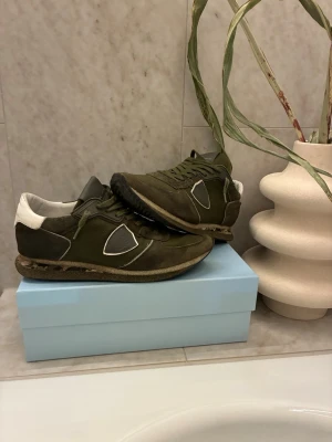 Olivgröna Philippe Model sneakers - Säljer ett par olivgröna Philippe Model sneakers med vita detaljer och logga på sidan. Skorna har snörning, rund tå och platt sula. Materialmix av mocka och textil ger en schysst streetkänsla. Perfekta för dig som gillar stilrena men ändå unika sneakers.