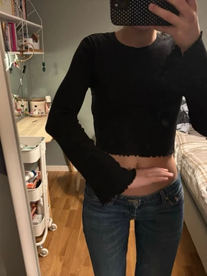 Svart croppad långärmad topp - Säljer en svart croppad topp med långa ärmar och vågiga kanter vid ärmslut och nederkant. Toppen har en enkel, stilren design och är perfekt att matcha med jeans eller kjol. Materialet känns mjukt och stretchigt för en bekväm passform.