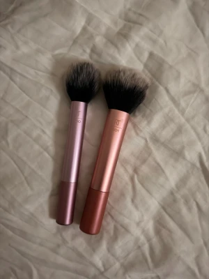 Fyra sminkborstar i metallic och nude - Säljer två sminkborstar från Real Techniques och två från flaer båda inköpta från kicks. Två har metallicrosa och kopparfärgade handtag med täta, mjuka borst. De andra två har nude och ljusrosa handtag, en är större och fluffig, den andra är en mindre solfjäderborste. Perfekta för puder, rouge eller highlighter.