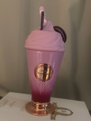 Armaf Yummy Pink parfym milkshake - Superfin parfymflaska från Armaf i form av en milkshake med rosa och lila toner, dekorerad med ett lock som ser ut som vispad grädde, ett sugrör och en macaron. Flaskan har en metallisk botten i roséguld och en rund etikett framtill. (Mer än 95% kvar) 