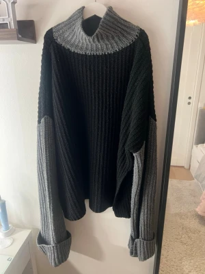 Svart och grå stickad polotröja - Säljer en oversized stickad tröja med polokrage i grått och svart. Tröjan har breda ribbstickade ärmar i grått och svart, samt en hög, mysig krage. Perfekt för kalla dagar och riktigt skön att bära.